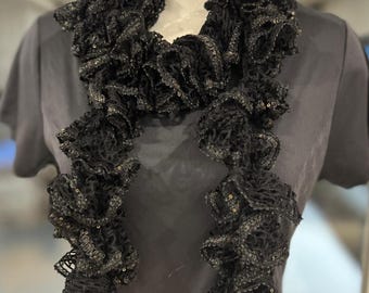 May include: A black ruffled scarf with a delicate lace pattern. The scarf is made of a soft, lightweight material and is perfect for adding a touch of elegance to any outfit.