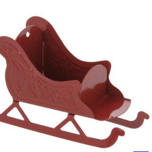 May include: A red metal sleigh with decorative floral detailing. The sleigh has curved runners and a seat. A small hole is at the top of the back of the sleigh. This decorative item is perfect for holiday decor.