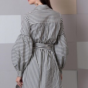May include: A long-sleeved, striped shirt with a tie belt. The shirt has a relaxed fit and features a button-up collar and long, puffy sleeves.