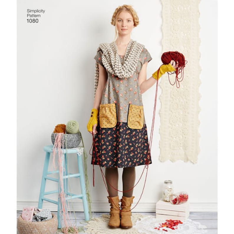 May include: A woman in a floral dress with mustard pockets and gloves, holding red yarn. The dress is paired with a chunky knit scarf. A light blue stool holds yarn balls. The text "Simplicity Pattern 1080" is visible.