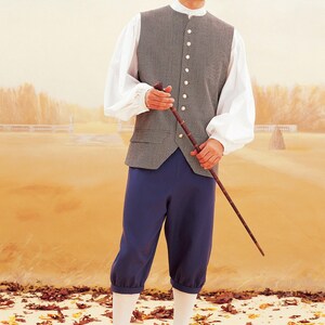 Puede incluir: Un hombre con un chaleco gris, camisa blanca y pantalones azules. Est&aacute; sosteniendo un bast&oacute;n y de pie sobre un lecho de hojas de oto&ntilde;o.