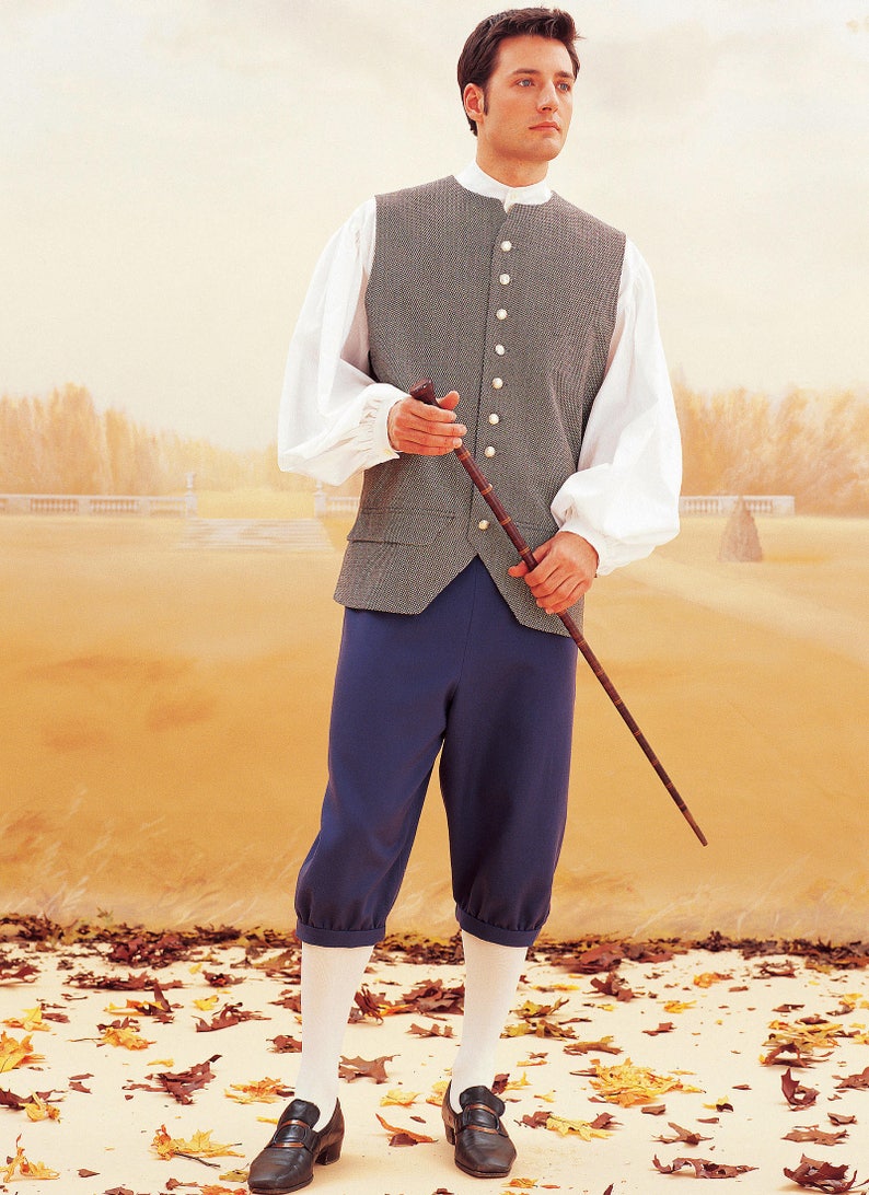 Puede incluir: Un hombre con un chaleco gris, camisa blanca y pantalones azules. Est&aacute; sosteniendo un bast&oacute;n y de pie sobre un lecho de hojas de oto&ntilde;o.