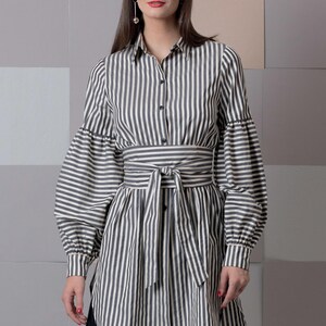 May include: A long-sleeved, striped shirt dress with a black and white pattern. The dress has a tie belt at the waist and a button-up front.