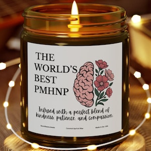 May include: A lit candle in a glass jar with a label that reads "THE WORLD'S BEST PMHNP" with a brain and flower graphic. The candle sits on a wooden coaster, with a guitar and book in the background.