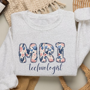 May include: A light gray crewneck sweatshirt featuring the text MRI technologist. The letters MRI are filled with a floral pattern of blue, pink, and white flowers. The word technologist is written below in a dark blue cursive script font.