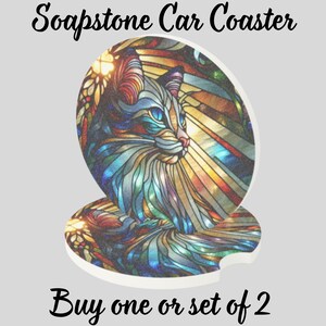 May include: Soapstone car coasters with a stained-glass cat design. The coasters feature a colorful cat portrait in shades of blue, gold, and red. The text "Buy one or set of 2" is displayed below the coasters.