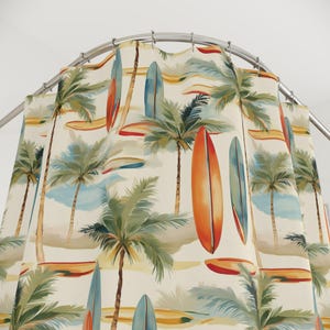 May include: A shower curtain with a tropical beach design. It features palm trees, surfboards, and a watercolour-style background in orange, blue, green, and beige. The curtain is suspended from a curved metal rail.