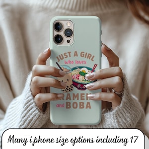 Puede incluir: Funda de iPhone verde claro con el texto "JUST A GIRL who loves RAMEN and BOBA". El diseño incluye ilustraciones de té boba y ramen. La funda la sostiene una persona que lleva un jersey color crema.