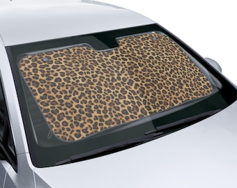 May include: A car windshield sunshade with a leopard print design. The sunshade is brown and tan with dark brown spots, and is installed in a silver car. The sunshade covers the entire windshield.
