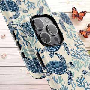 May include: A phone case featuring a repeating pattern of blue sea turtles and coral on a cream background. The case has a black border around the camera lenses and a glossy finish. Two orange butterflies are in the background.