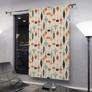 May include: A cream-colored curtain with a repeating mid-century modern design. The pattern features stylized shapes in orange, teal, and navy blue. The curtain is hanging in front of a window, adding a pop of color to the room.