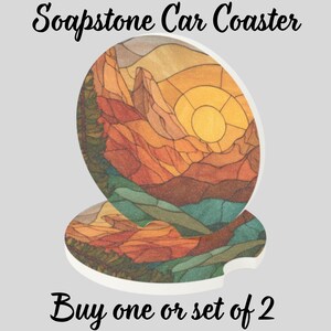 May include: Two soapstone car coasters with a landscape design featuring mountains, a sun, and trees in shades of orange, yellow, and green. The coasters have a white border and a curved cutout for easy removal. Text on the image reads "Soapstone Car Coaster" and "Buy one or set of 2."