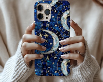 Op de afbeelding: Een blauwe telefoonhoes met een glas-in-lood ontwerp met halve manen en sterren. De hoes heeft een mozaïekachtig patroon met gouden accenten. De telefoonhoes wordt vastgehouden door een persoon die een crèmekleurige trui draagt.