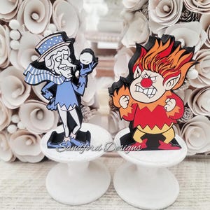 May include: Two cartoon character figurines, one resembling a snowman and the other a fiery imp, stand on white pedestals. The snowman figure is in blue and white, holding a snowball. The imp is red and orange, with an angry expression. The base reads "Sandford Designs."