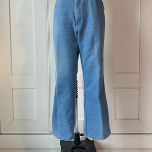 May include: Pale blue denim trousers with a flared leg. The high-waisted jeans have a button and zip fastening. The trousers are displayed on a mannequin against a white backdrop.