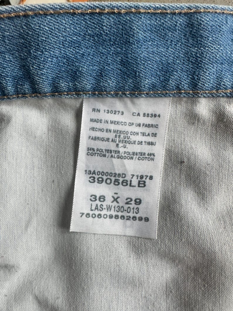 May include: Close-up of light blue denim fabric with a white tag. The tag shows text including "36 X 29" and "39056LB". The tag also indicates the item was made in Mexico.
