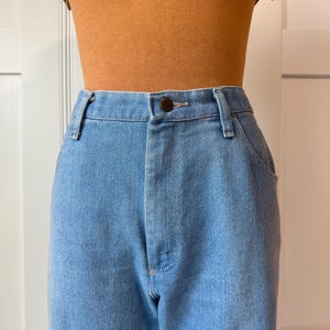 May include: Light blue denim jeans with a button closure and belt loops. The jeans are paired with a brown top. The jeans have a classic, straight-leg fit.