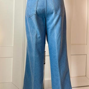May include: Light blue denim trousers with a wide leg design. The trousers have two back pockets and a classic five-pocket style. The jeans are a medium wash and appear to be vintage.