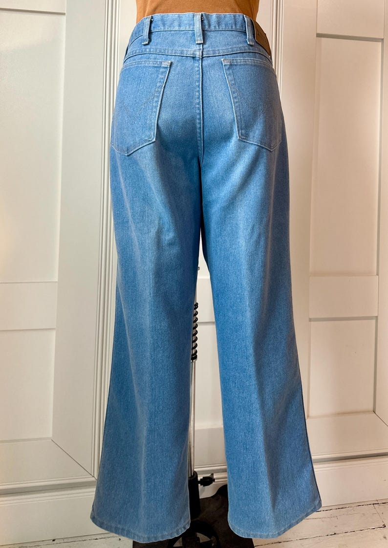May include: Light blue denim trousers with a wide leg design. The trousers have two back pockets and a classic five-pocket style. The jeans are a medium wash and appear to be vintage.