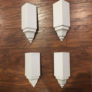 May include: Four white corner blocks with decorative trim. The blocks are made of a smooth, white material and have a simple, elegant design.