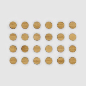 May include: A set of 25 round wooden discs, arranged in a grid pattern on a white background. The discs are a light brown colour and have a smooth, polished finish.