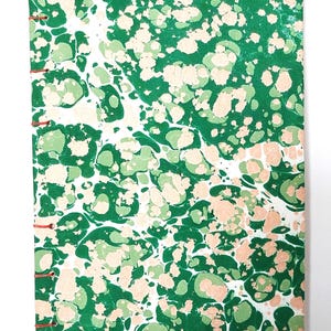 May include: A handmade journal with a marbled cover. The cover displays a pattern of green, light green, and peach-coloured swirls on a white background. The pages are bound with red thread.