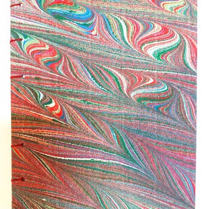 Op de afbeelding: Een handgemaakt notitieboek met een marmeren papieren omslag. De omslag heeft een wervelend patroon van rode, groene, blauwe en witte kleuren. Het notitieboek is gebonden met rode draad langs de rug, de pagina's zijn zichtbaar.