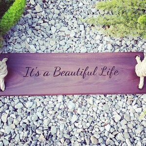 Puede incluir: Un columpio de madera con cuerda y las palabras "It's a Beautiful Life" grabadas en el asiento.