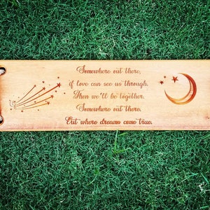 Puede incluir: Un letrero de madera con una cita sobre el amor y los sue&ntilde;os. El letrero est&aacute; decorado con una luna creciente y estrellas fugaces. La cita dice: "En alg&uacute;n lugar ah&iacute; fuera, si el amor puede vernos a trav&eacute;s. Entonces estaremos juntos. En alg&uacute;n lugar ah&iacute; fuera. Donde los sue&ntilde;os se hacen realidad."