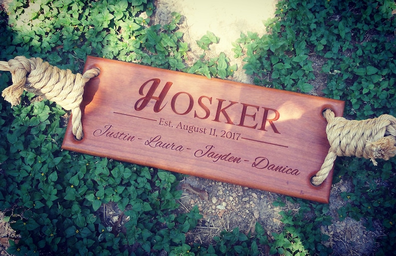 Puede incluir: Un columpio de madera con asas de cuerda, personalizado con el apellido "HOSKER" y el texto "Est. August 11, 2017" junto con los nombres "Justin - Laura - Jayden - Danica".