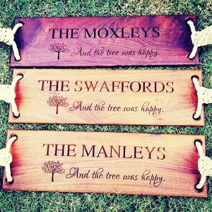 Puede incluir: Tres columpios de madera con asas de cuerda. Cada columpio tiene un nombre personalizado y el texto "And the tree was happy." Los nombres son "The Moxleys", "The Swaffords" y "The Manleys".