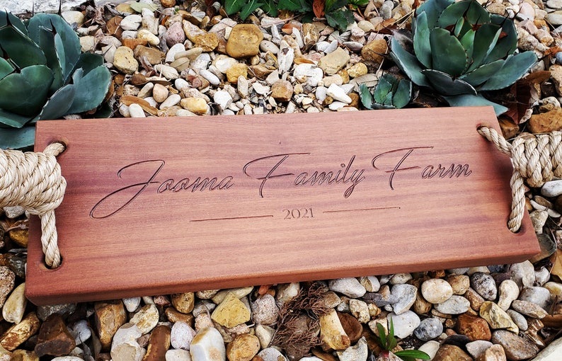 Puede incluir: Un columpio de madera con asas de cuerda, grabado con el texto "Joama Family Farm 2021".