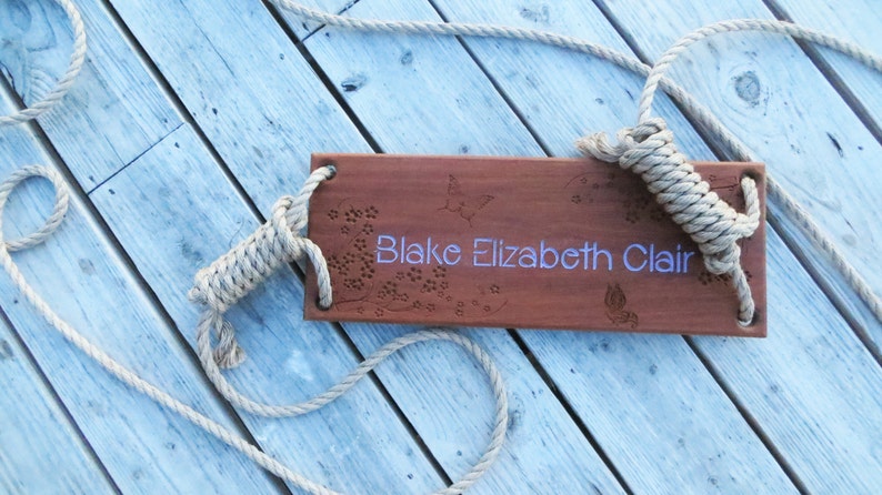 Puede incluir: Un columpio de madera con un acabado de madera natural y cuerda. El columpio est&aacute; grabado con el nombre "Blake Elizabeth Clair".