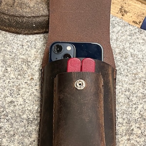 May include: A brown leather phone case with a flap that opens to reveal a phone and a small red tool. The case has a snap closure and a distressed look.