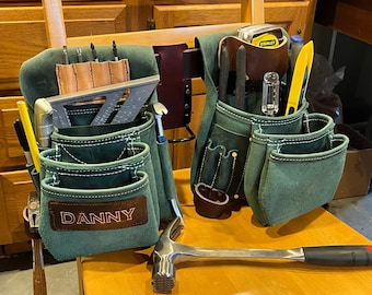 May include: Two green leather tool belts with various pockets and tools, including a level, a tape measure, and a hammer. The belt on the left has the name "DANNY" embroidered on it.