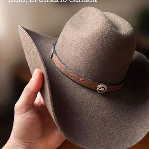 May include: A brown cowboy hat with a leather band featuring decorative stitching and silver-toned star-shaped accents. The hat has a wide brim and is made of a felt-like material. The text "Photo by our client, Dino, in Ontario Canada" is visible.