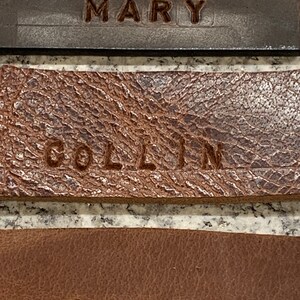 Pu&ograve; includere: Tre targhette in pelle con i nomi "MARY", "COLLIN" e "GARY" incisi in lettere marroni.
