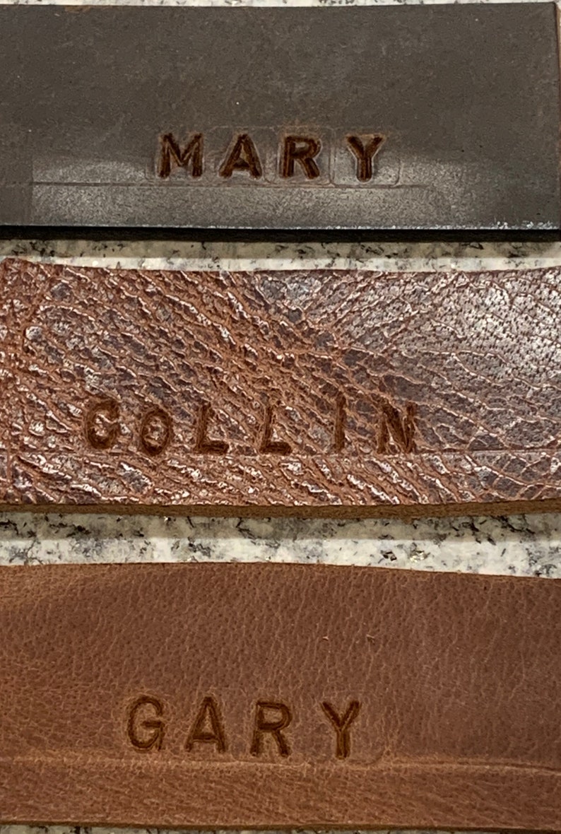 Pu&ograve; includere: Tre targhette in pelle con i nomi "MARY", "COLLIN" e "GARY" incisi in lettere marroni.