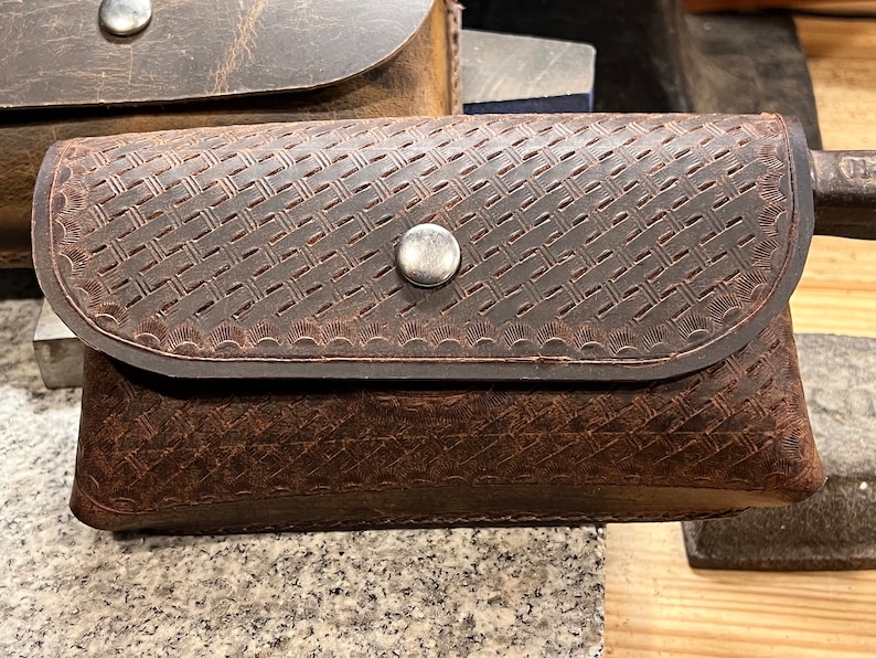 May include: A brown leather pouch with a woven pattern and a silver snap closure.