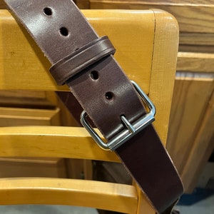 May include: A brown leather strap with a silver buckle. The strap is on a wooden surface.
