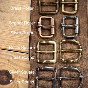 May include: A collection of eight metal belt buckles arranged in two columns. The set includes antique brass, brass roller, copper roller, silver roller, brass square, brass round, silver square, and silver round styles with labels for each.
