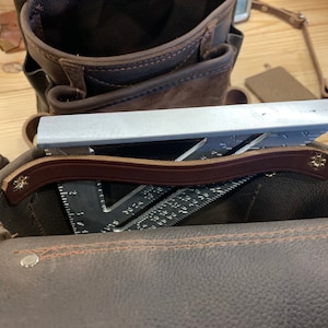 May include: A brown leather tool bag with a brown leather strap and a silver metal ruler inside.