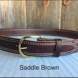 Pu&ograve; includere: Una cintura in pelle marrone con cuciture bianche e una fibbia dorata. La cintura &egrave; etichettata "Saddle Brown".