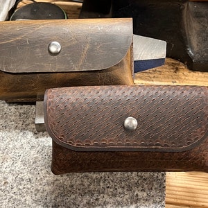 May include: Two brown leather pouches with snap closures. The pouch on the left has a smooth surface and the pouch on the right has a woven pattern.