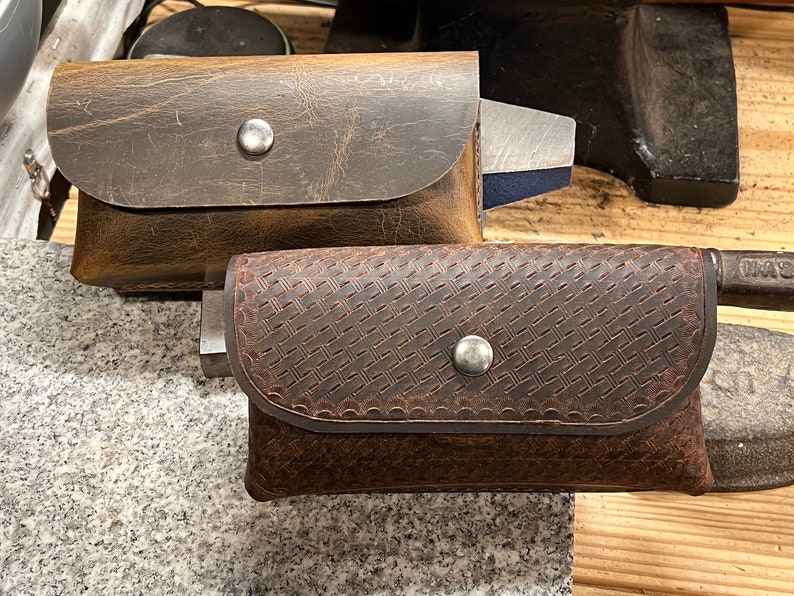 May include: Two brown leather pouches with snap closures. The pouch on the left has a smooth surface and the pouch on the right has a woven pattern.
