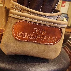 May include: A tan suede leather tool pouch featuring a dark brown leather patch embossed with the name ED CROFTON. The pouch has white contrast stitching along the top edges and multiple compartments for holding various tools securely in place.