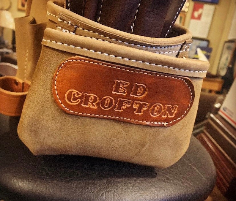 May include: A tan suede leather tool pouch featuring a dark brown leather patch embossed with the name ED CROFTON. The pouch has white contrast stitching along the top edges and multiple compartments for holding various tools securely in place.
