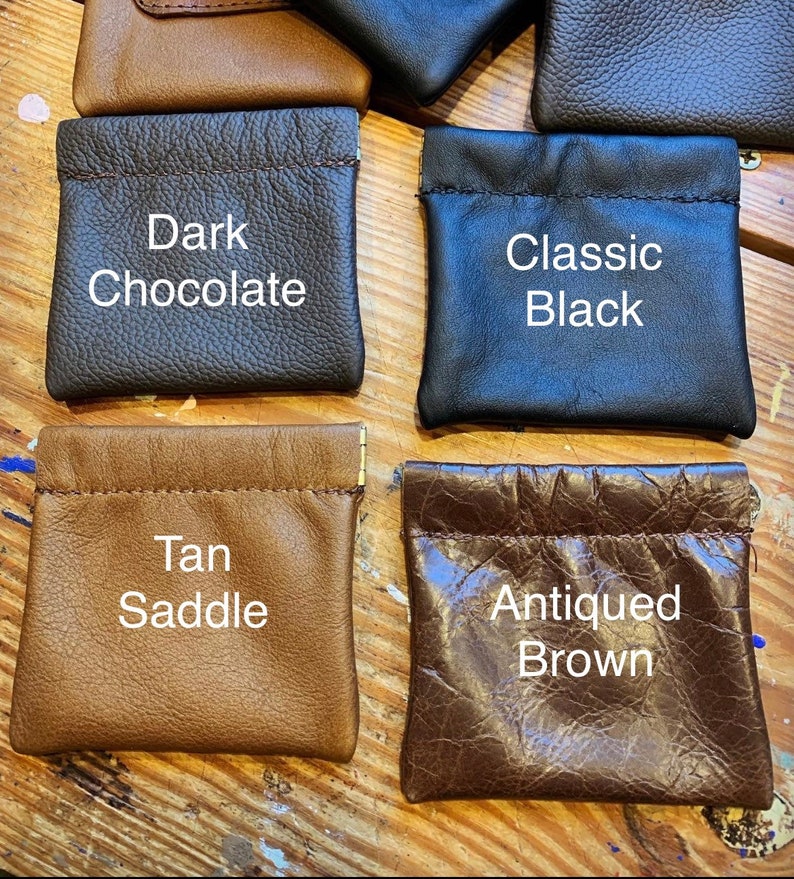 Peut inclure: Quatre petites pochettes en cuir de diff&eacute;rentes couleurs et textures. Les pochettes sont &eacute;tiquet&eacute;es "Chocolat Noir", "Noir Classique", "Selle Tan" et "Brun Antique".