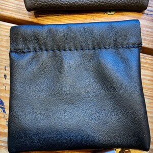 Peut inclure: Une pochette en cuir noir avec une fermeture &agrave; cordon. La pochette est faite de cuir souple et doux et a une texture lisse et uniforme.