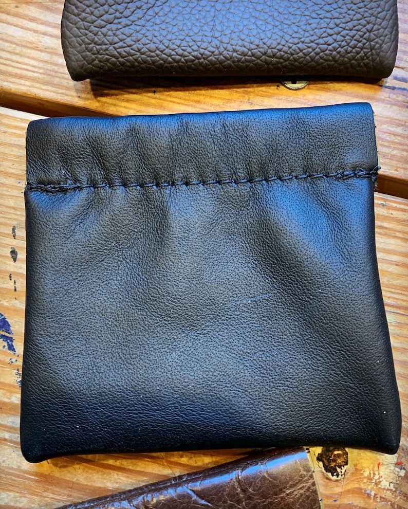 Peut inclure: Une pochette en cuir noir avec une fermeture &agrave; cordon. La pochette est faite de cuir souple et doux et a une texture lisse et uniforme.